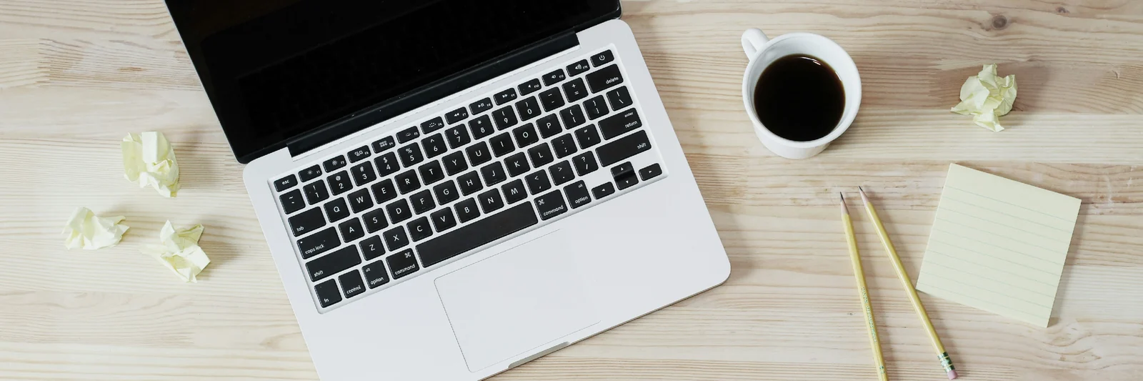 Scrivania vista dall'alto con laptop, tazza di caffè, matite e appunti, l'atmosfera concreta dello studio