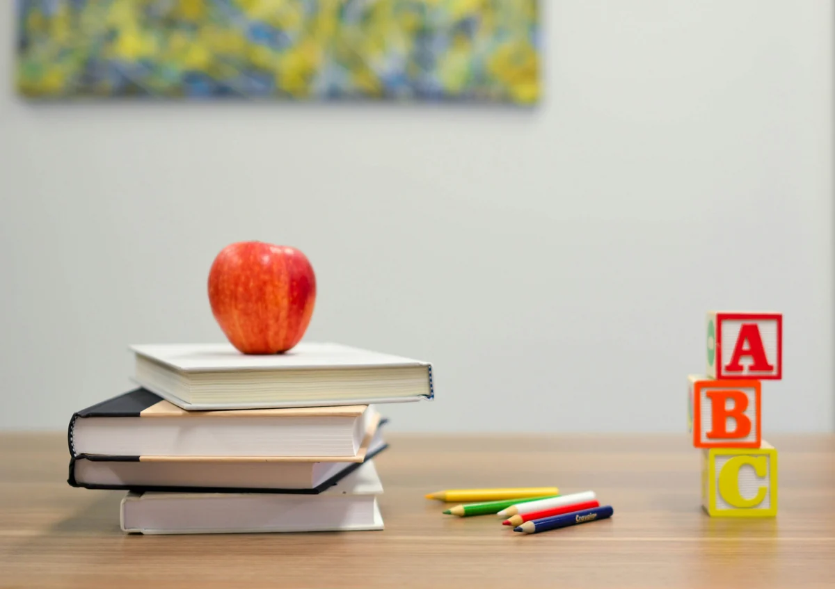 Manifesto Starry Mind Academy: libri, mela e cubi ABC su una scrivania, simboli di educazione inclusiva e apprendimento consapevole.