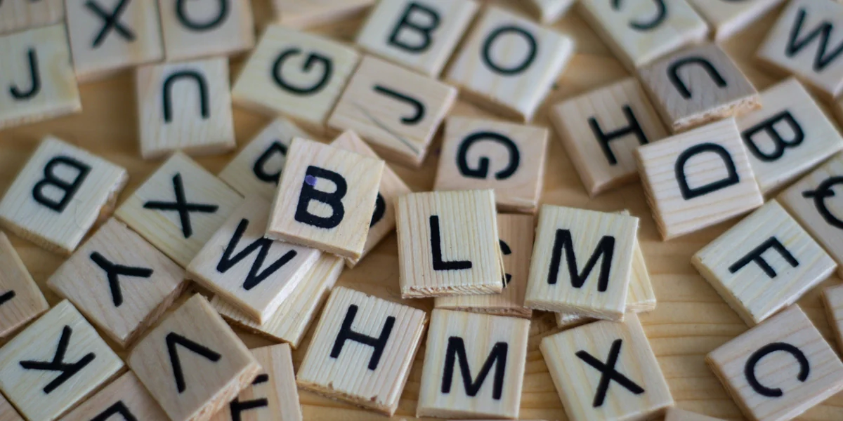 Tessere di legno con le lettere dell'alfabeto sparse su un tavolo, alcune a fuoco e altre sfocate.